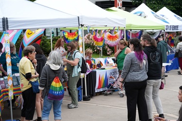several people walk past popup tents waving pride flags